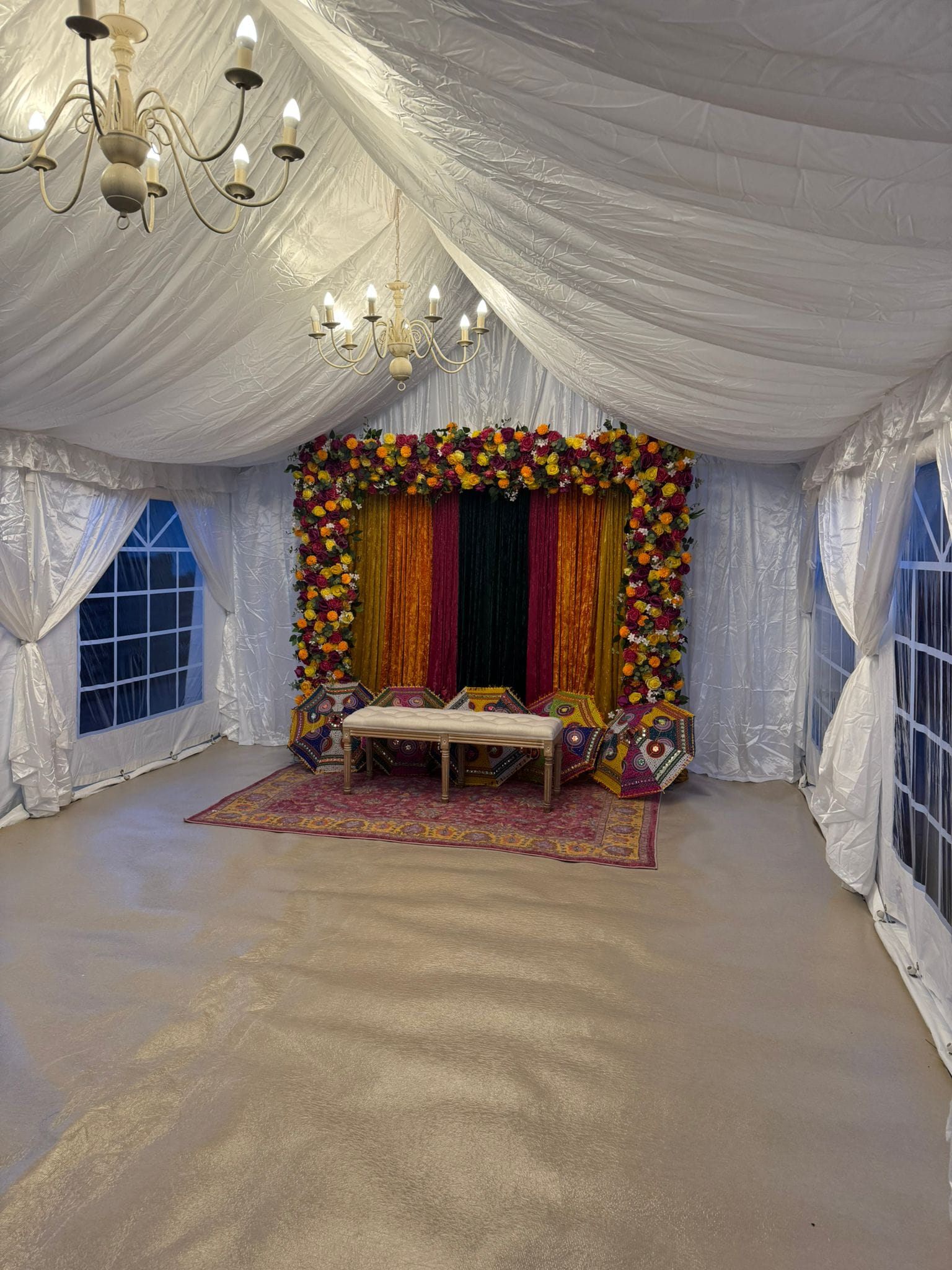 Mehndi marquee setup with floral backdrop, draped fabrics and chandeliers in a 4m by 6m London marquee