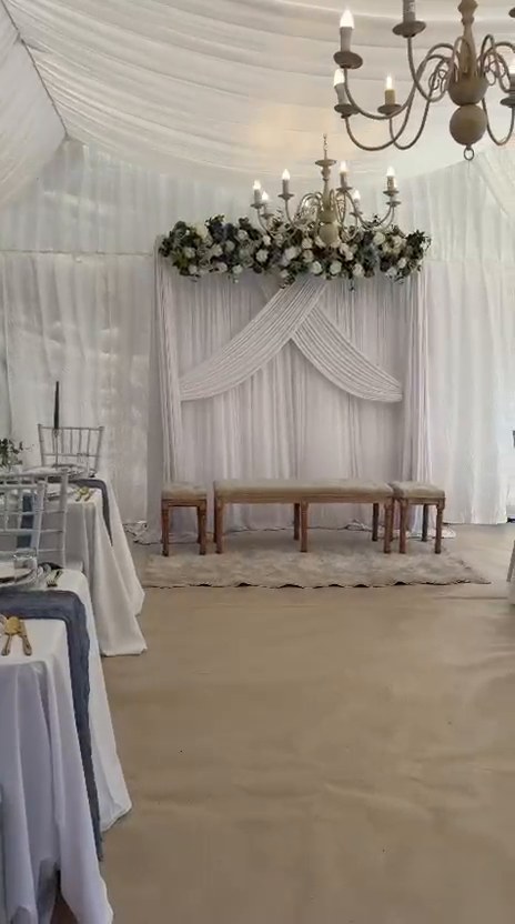 Nikkah ceremony stage with floral chandelier arrangement, draped backdrop and seating benches in a marquee